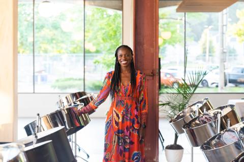 Woman in a floral dress standing between two rows of steel pan instruments